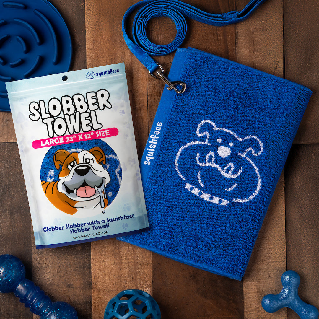 Blue towel with dog logo, packaging of 'Slobber Towel', and dog toys on a wooden surface